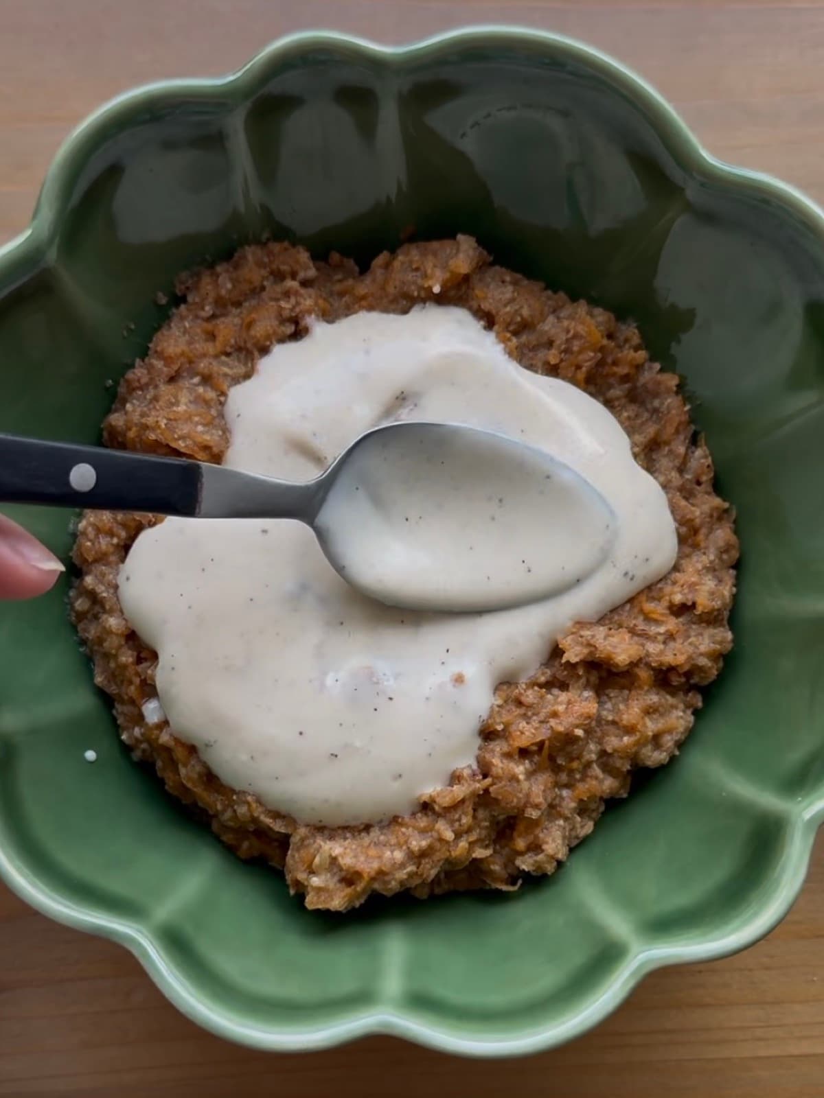 Un cucchiaio che spalma la glassa di yogurt alla vaniglia sul porridge alla torta di carote in una ciotola verde