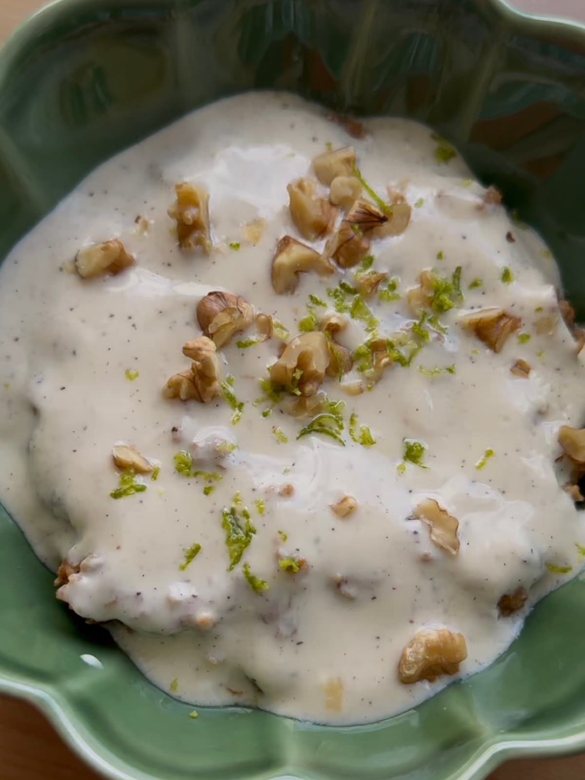 Una ciotola di porridge alla torta di carote ricoperto di glassa di yogurt alla vaniglia, noci tritate e scorza di lime, in una ciotola verde smerlata