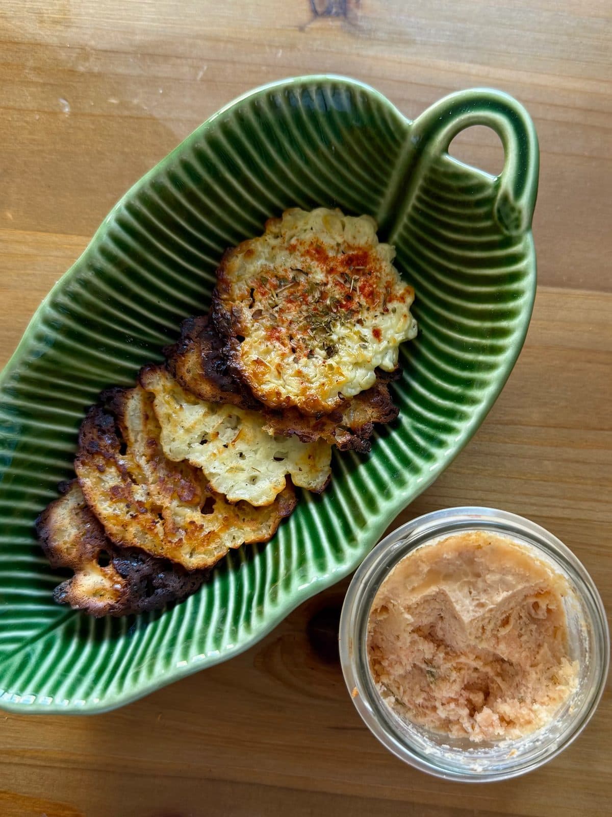 Golden cottage cheese chips topped with paprika and dried oregano in a green leaf-shaped dish on a wooden table