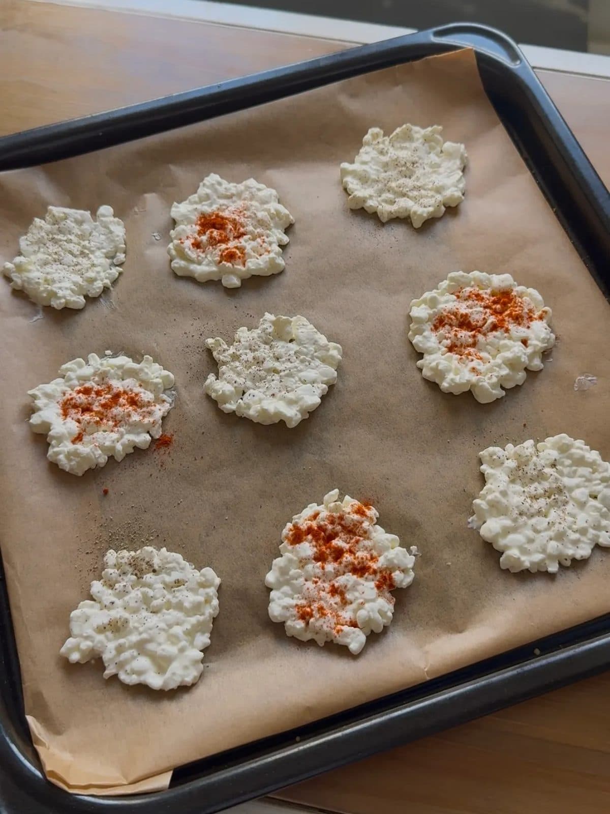 De petits ronds de cottage cheese sur une plaque recouverte de papier cuisson, certains saupoudrés de paprika, avant la cuisson