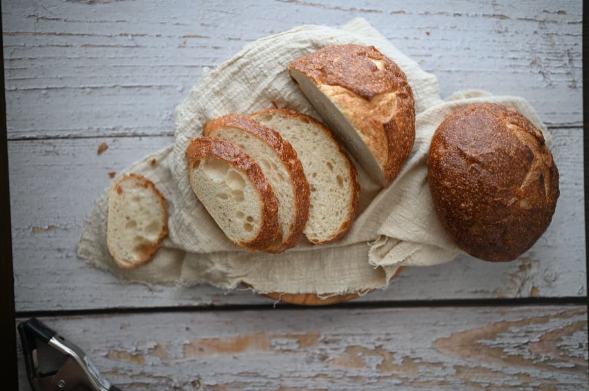 Scheiben von knusprigem Sauerteigbrot auf einem Leinentuch neben einem ganzen Laib, von oben fotografiert